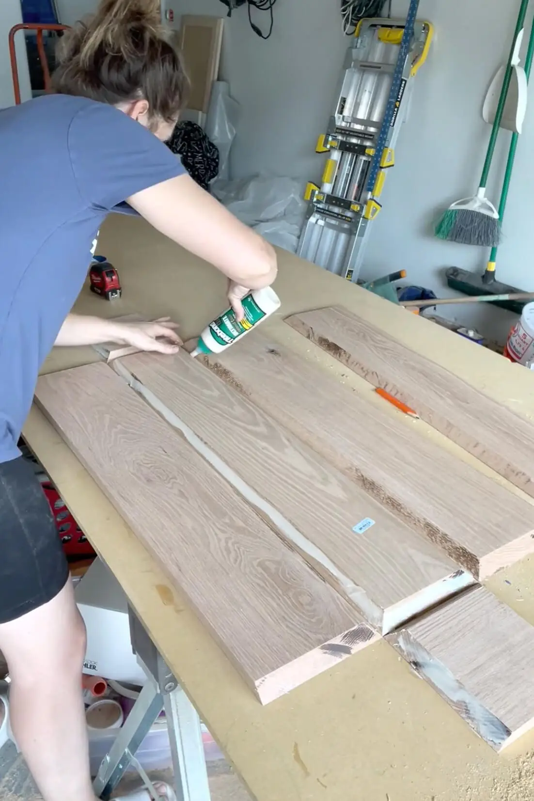 Applying wood glue along the beveled edges of oak boards to assemble a DIY fireplace mantel.